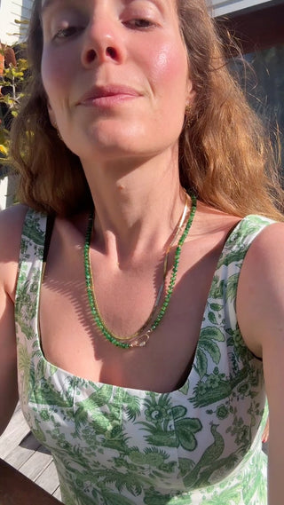 Woman wearing a green and white patterned top with a necklace outdoors.