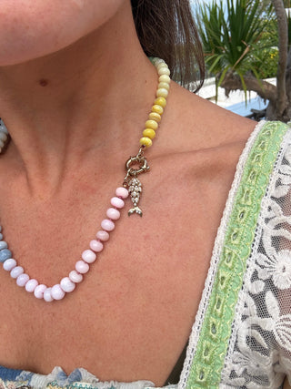 Necklace with pink and yellow beads and a mermaid charm worn by a person outdoors.