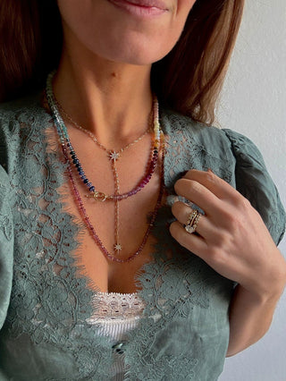 Close-up of a person wearing multiple necklaces and a ring, with a blurred background.