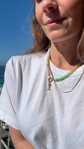 Person wearing a white t-shirt with a necklace against a blue sky background