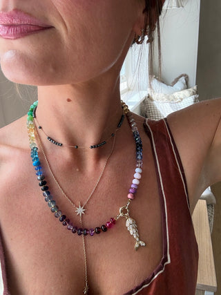 Close-up of a person wearing multiple necklaces with colorful beads and a fish charm.