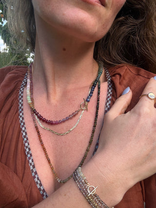 Close-up of a person wearing multiple necklaces and bracelets with a blurred background