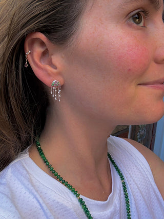 Close-up of a woman wearing a white gold jellyfish earring, diamond hoops and an emerald necklace.